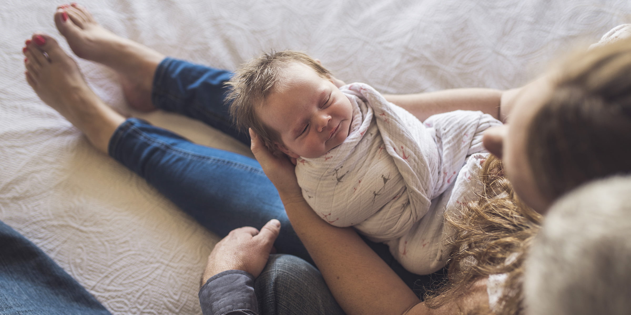 Overhead view of parents with newborn daughter sitting on bed at home